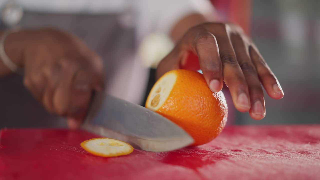 el hombre negro corta la naranja en la mesa de primer plano. el chef afroamericano corta frutas cítricas dulces para la cocina de postres en la cocina. ingrediente natural de platos exóticos