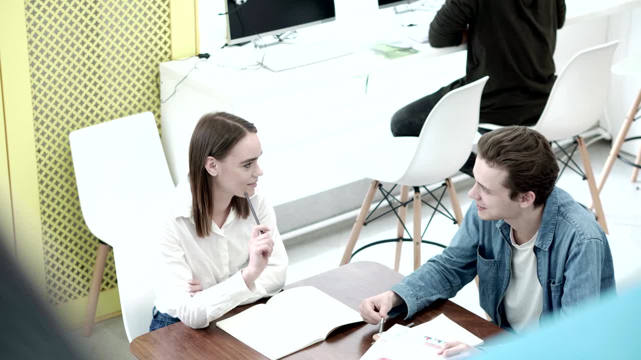 대학 소년과 소녀는 공동 작업실에서 책상에 앉아서 숙제를 즐겁게 이야기합니다.