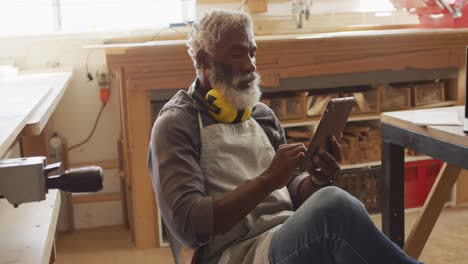 African-american-male-carpenter-using-digital-tablet-sitting-in-a-carpentry-shop