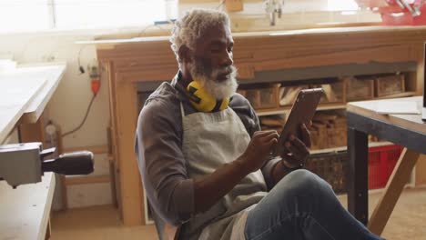 african american male carpenter using digital tablet sitting in a carpentry shop