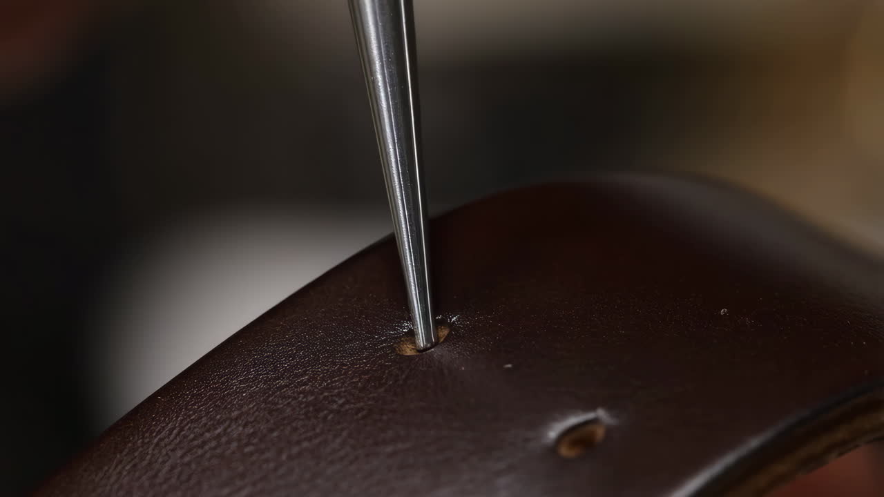 Close-up of a tool piercing a hole in brown leather