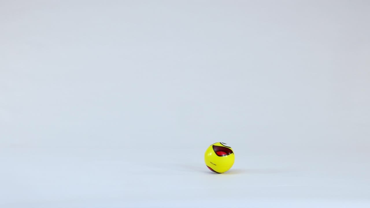 Una palla gialla con una faccia sorridente rimbalza ripetutamente su uno sfondo bianco semplice da studio