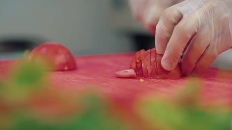 cook cuts a fresh tomato for a salad with a knife