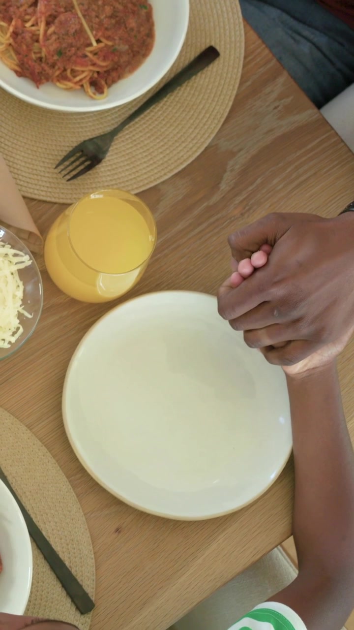 Vídeo vertical: Menino estendendo a mão, pai de vermelho segurando a mão à mesa antes da refeição com suco, com espaço para texto.