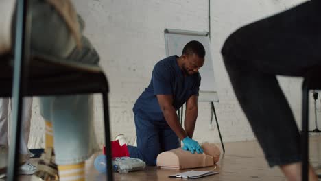 bottom view: a black male doctor in blue uniform conducts a practice session showing artificial respiration on a medical mannequin