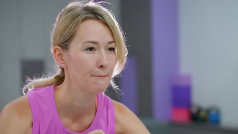 primer plano de una mujer joven de color rosa ajustando la postura con determinación, la luz brilla detrás de ella, creando un brillo sutil, el fondo borroso presenta equipos de gimnasio