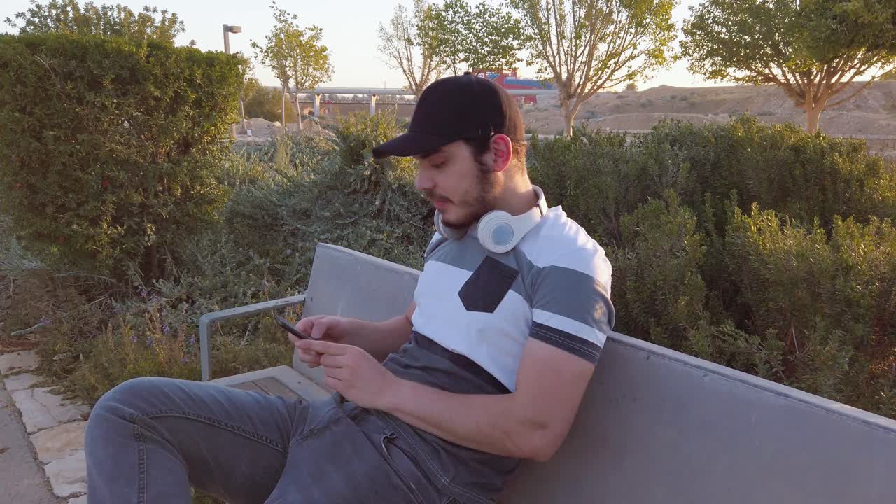 Smiling young man, listening music, checks his mobile, in a park