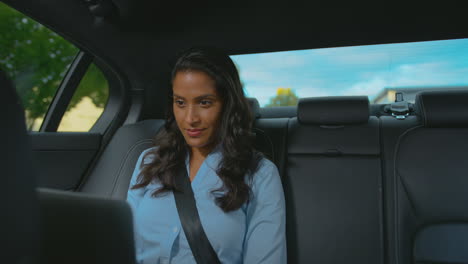 mature businesswoman sitting in back seat of taxi or car working on laptop