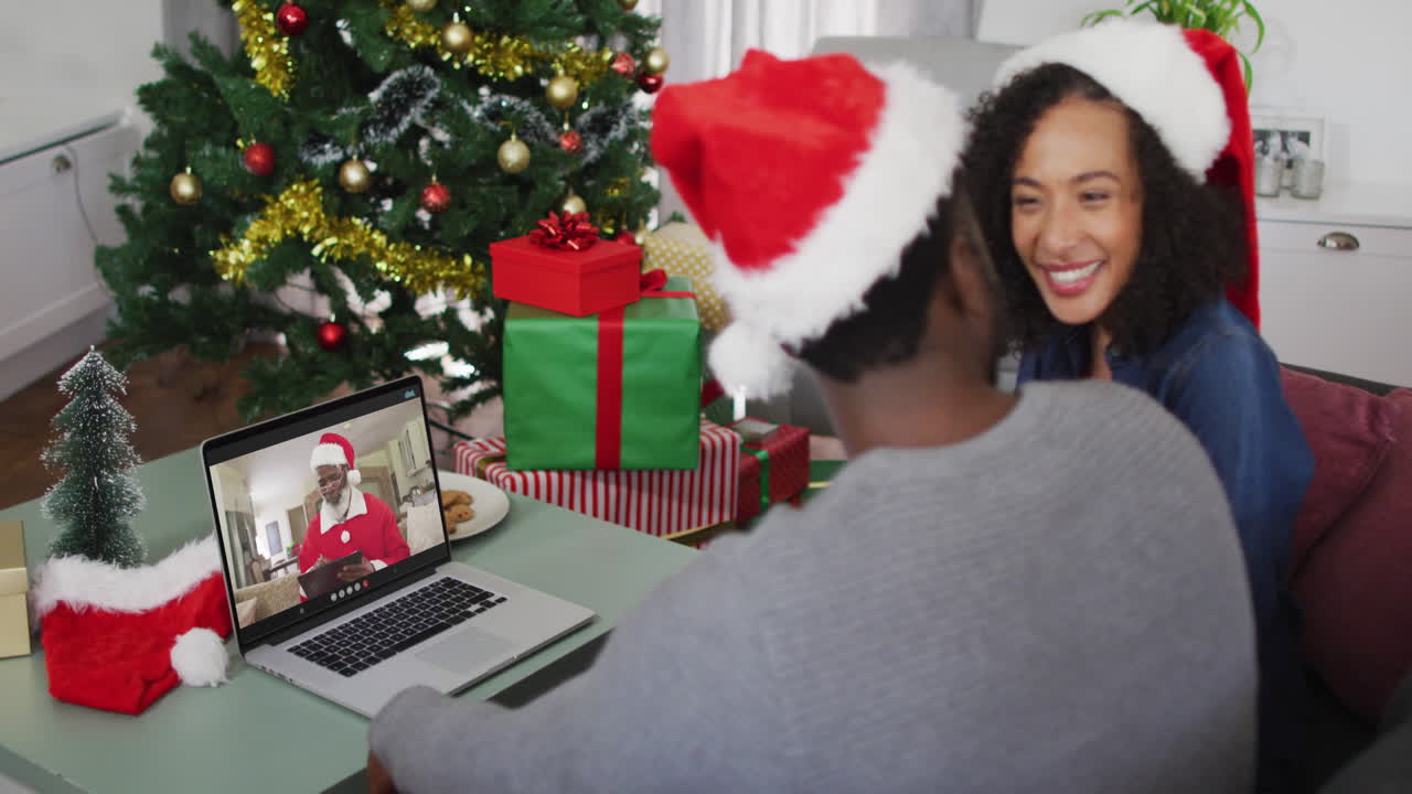 pareja afroamericana con sombreros de santa haciendo una videollamada en una computadora portátil en casa durante la navidad