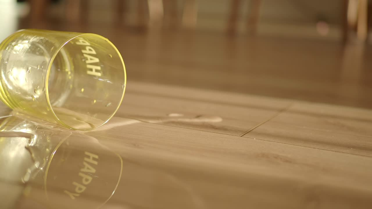 Spilled water from a 'Happy' glass on a wooden floor