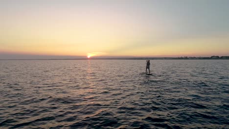 paddleboarder paddling away into the sunset.