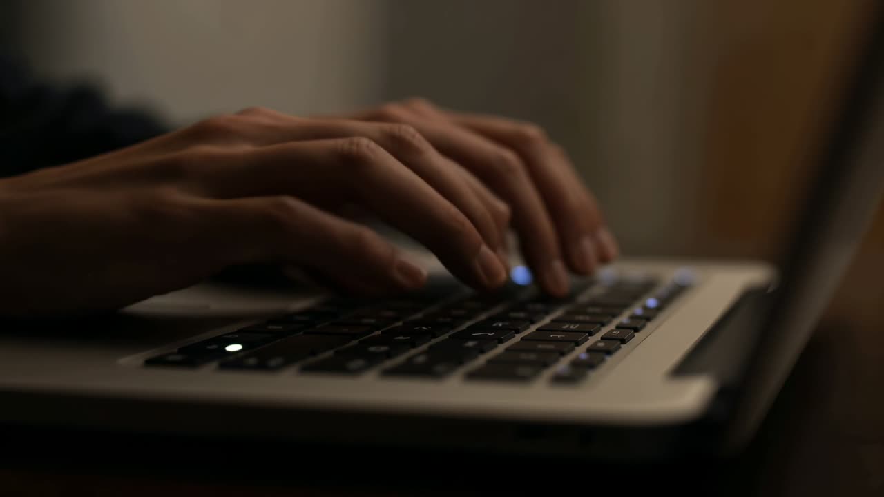 Hænder starter på baggrundsbelyst bærbart tastatur og skriver noter til teknologiarbejde, pauser, genoptager.