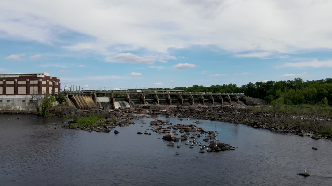 Close up of a river dam in Chippewa Falls in Wisconsin, with low river level and strong current of water rushing through, while cars drive over the bridge.