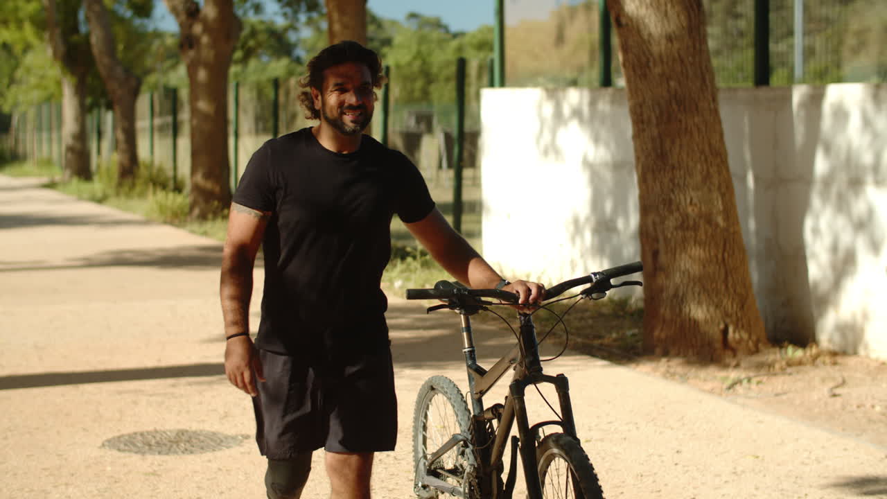 Uomo allegro con disabilità che percorre un sentiero spingendo la bicicletta.