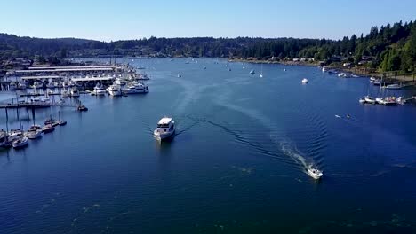 aerial, reverse, drone shot following boats leaving gig harbor, on a sunny day, in washington, usa