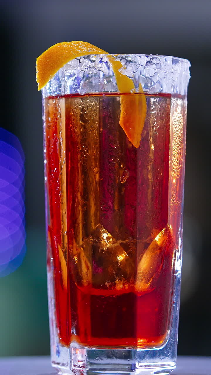 Little rotating table with red beverage. Beautiful cocktail with salt on glass top and orange peel. Close up. Blurred backdrop. Vertical video