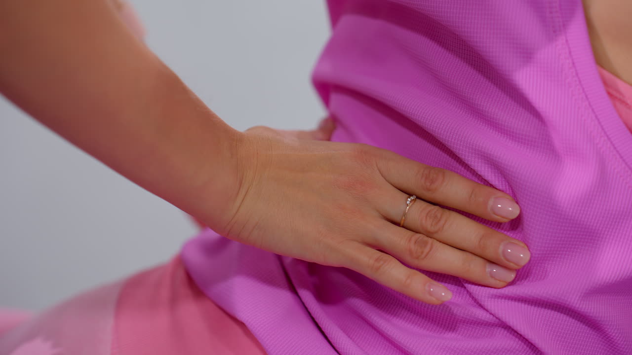 primer plano de manos ayudando a una mujer con ropa deportiva rosa mientras realiza un estiramiento de la columna vertebral, una mano lleva un anillo, y la otra un reloj inteligente, simbolizando la orientación profesional en un entorno de gimnasio