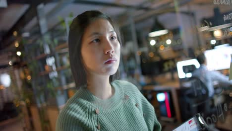 Focused-asian-casual-businesswoman-with-tablet-brainstorming-writing-on-office-glass-wall-at-night