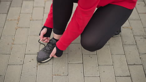 vista lateral de una atleta en cuclillas en un camino entrelazado atando su cordón derecho, enfoque de primer plano en las manos y el zapato, destacando la preparación y la dedicación para la actividad al aire libre en el fitness