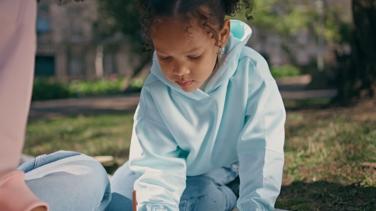 una chica encantadora pintando un álbum sentada en green meadow con su madre de cerca.