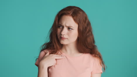 Doubtful-and-confused-redhead-girl-in-front-of-camera-on-turquoise-background.