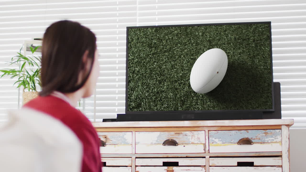 스크린 에 있는 경기장 에서 럭비 공 을 들고 tv 를 보는 백인 여자