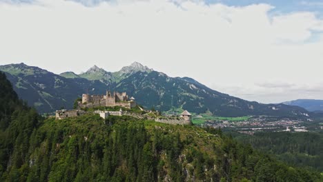 aerial view of ehrenberg castle in austria, atop a hill, overlooking mountains and a town below, on a cloudy day