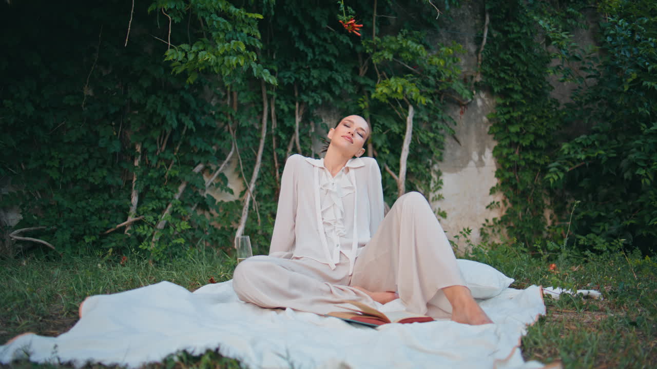 편안한 여성은 아름다운 녹색 유리잔에서 피크닉을 즐기고 있습니다. 자연에 와인을 가진 소녀