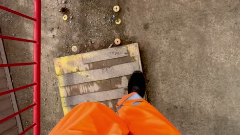 pov of feet walking wearing bright orange high visibility trousers at construction site