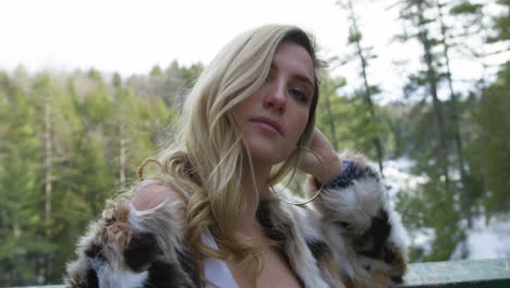 confident young blonde woman posing on an overlook, scenic winter forest in the background