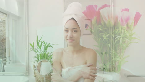 animation of pink flowers in vase over portrait of happy biracial woman wearing towel in bathroom