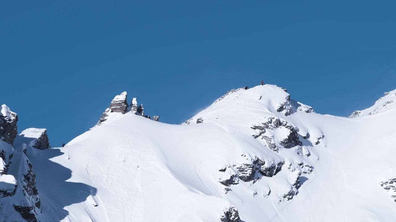 Freerider e scialpinisti che arrivano su una cima alpina innevata prima della discesa, radunandosi sulla cresta esposta per valutare le condizioni e scegliere le loro linee.