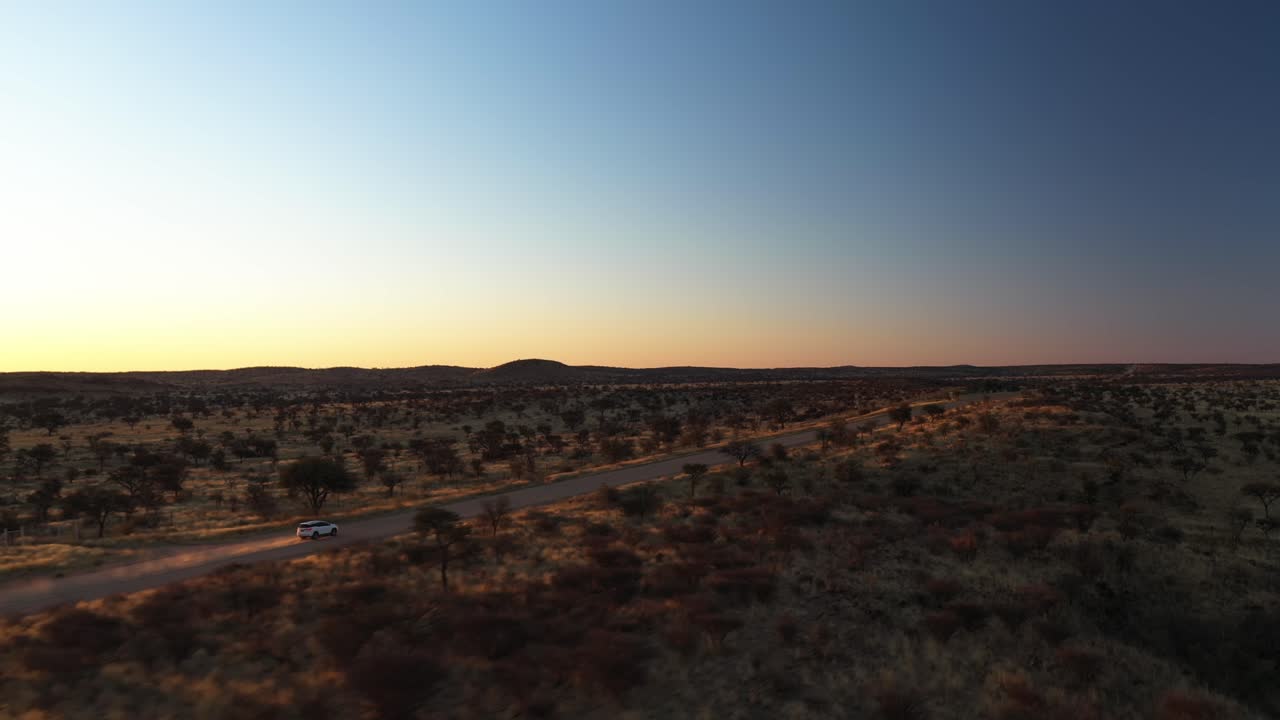 drone filmado siguiendo un suv blanco moviéndose a través de la lejana pradera, puesta de sol en namibia, áfrica