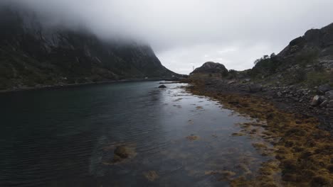 volando a lo largo de la orilla cerca del agua mirando, a la izquierda las montañas están cubiertas de niebla