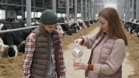 woman pouring fresh milk for teenage boy at farm