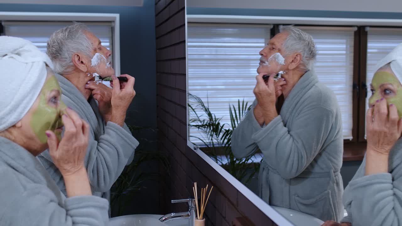 Nonna anziana che applica una maschera facciale e nonno che si rade con un rasoio manuale in bagno.