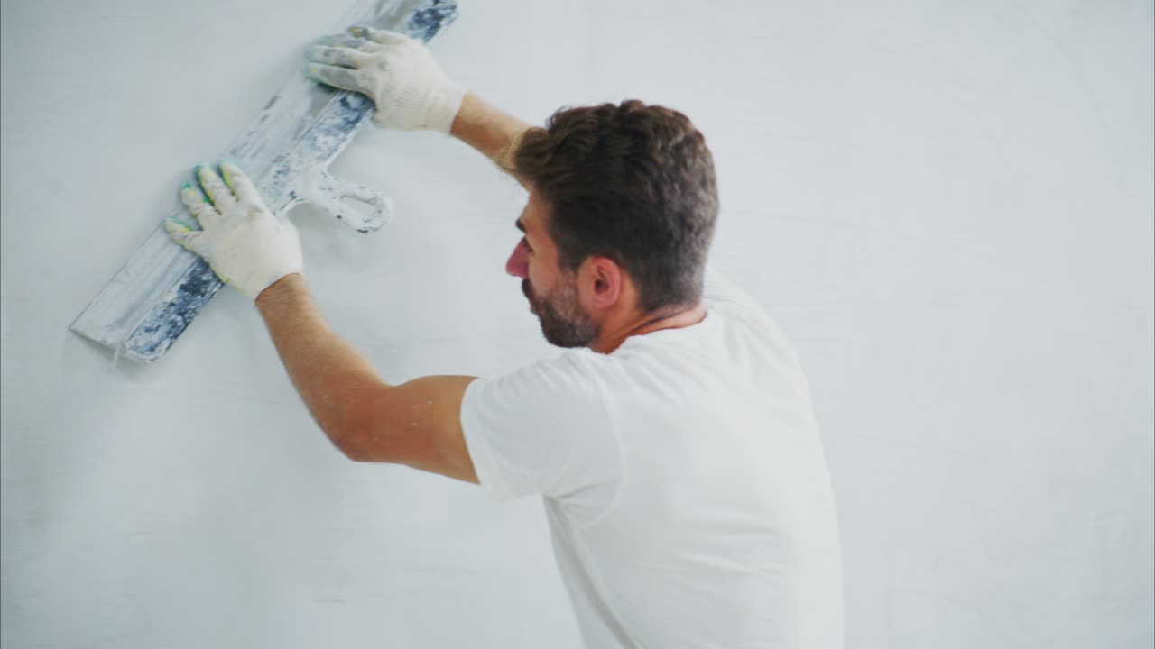 A Skilled Worker Applying Finishing Touches to a White Wall with a Smoothing Tool, Showcasing the Art of Wall Preparation in Home Improvement Projects