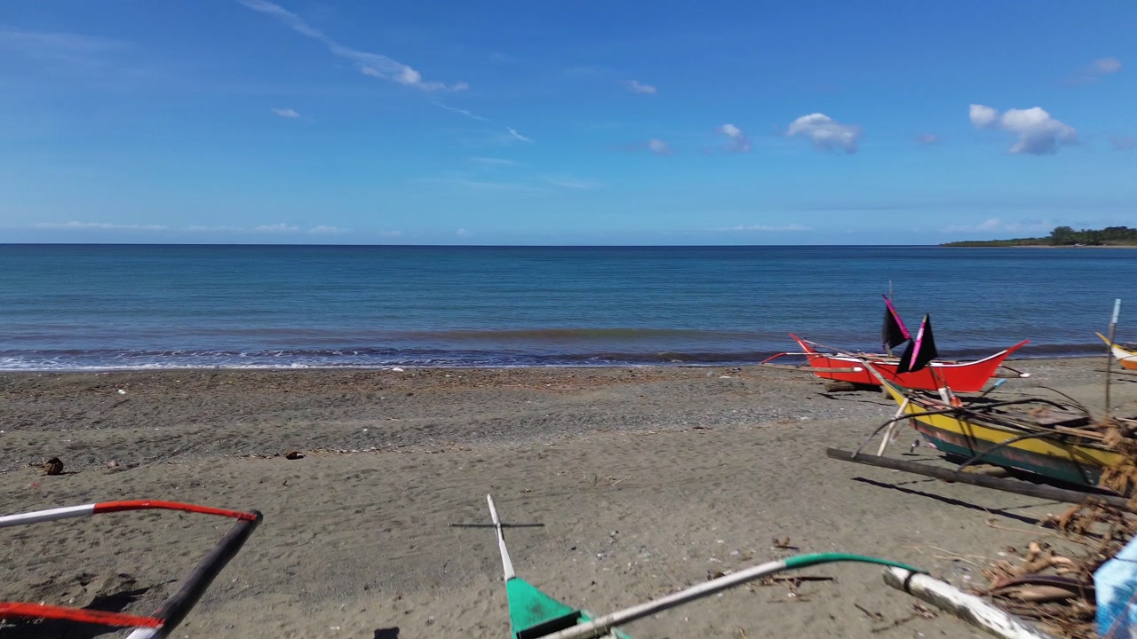 Cinematic aerial flyover of Odiongan Romblon Philippines showing small fishing boats resting on a sandy beach with palm trees blue ocean and clear sky on a sunny tropical day captured in smooth 4K