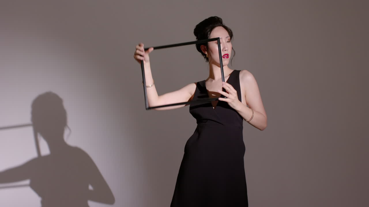 Asian Chinese woman entering studio manipulating square frame under spotlight creating silhouettes