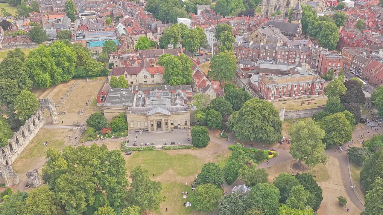Aerial over central York, England, showing the Yorkshire Museum, Museum Gardens, and the ruins of St Mary’s Abbey surrounded by historic city architecture and tree-lined paths