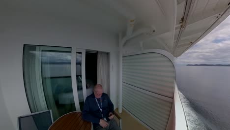 Man-reading-from-his-smartphone-sitting-on-the-balcony-of-a-cruise-ship-off-the-coast-of-Alaska