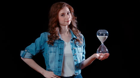 a young caucasian woman points at an hourglass and shakes her head