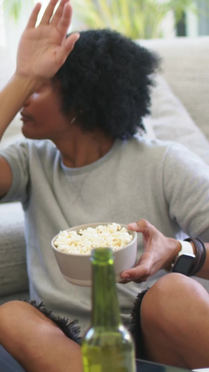 Vertikal video: Mand spiser popcorn, taler og gestikulerer på sofaen, holder skål og reagerer på skærm.