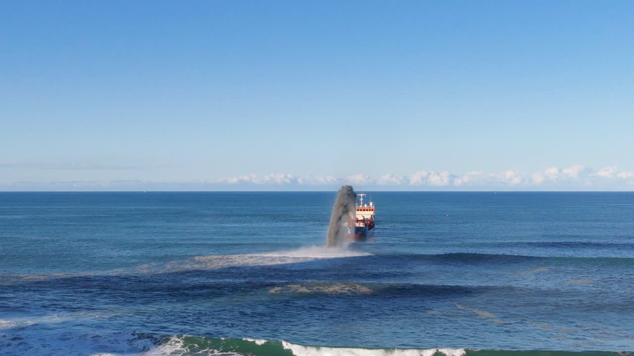 Aerial view of a dredging vessel dispersing sand into the ocean under clear skies at Gold Coast, Australia