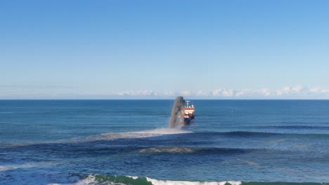 aerial view of a dredging vessel dispersing sand into the ocean under clear skies at gold coast, australia