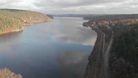 Drone-Volando-Sobre-El-Lago-Con-Reflejos-De-Nubes,-Carretera-Y-Ferrocarril-Al-Lado