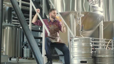 young brewer wearing a leather apron is tasting beer at a modern brewery