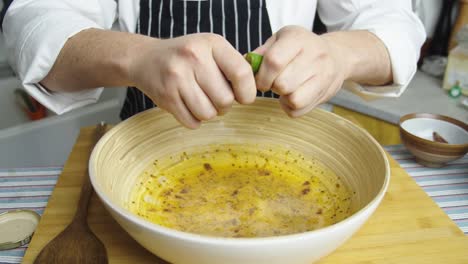 chef squeezes lime lemon juice into deep bowl with caesar salad sauce