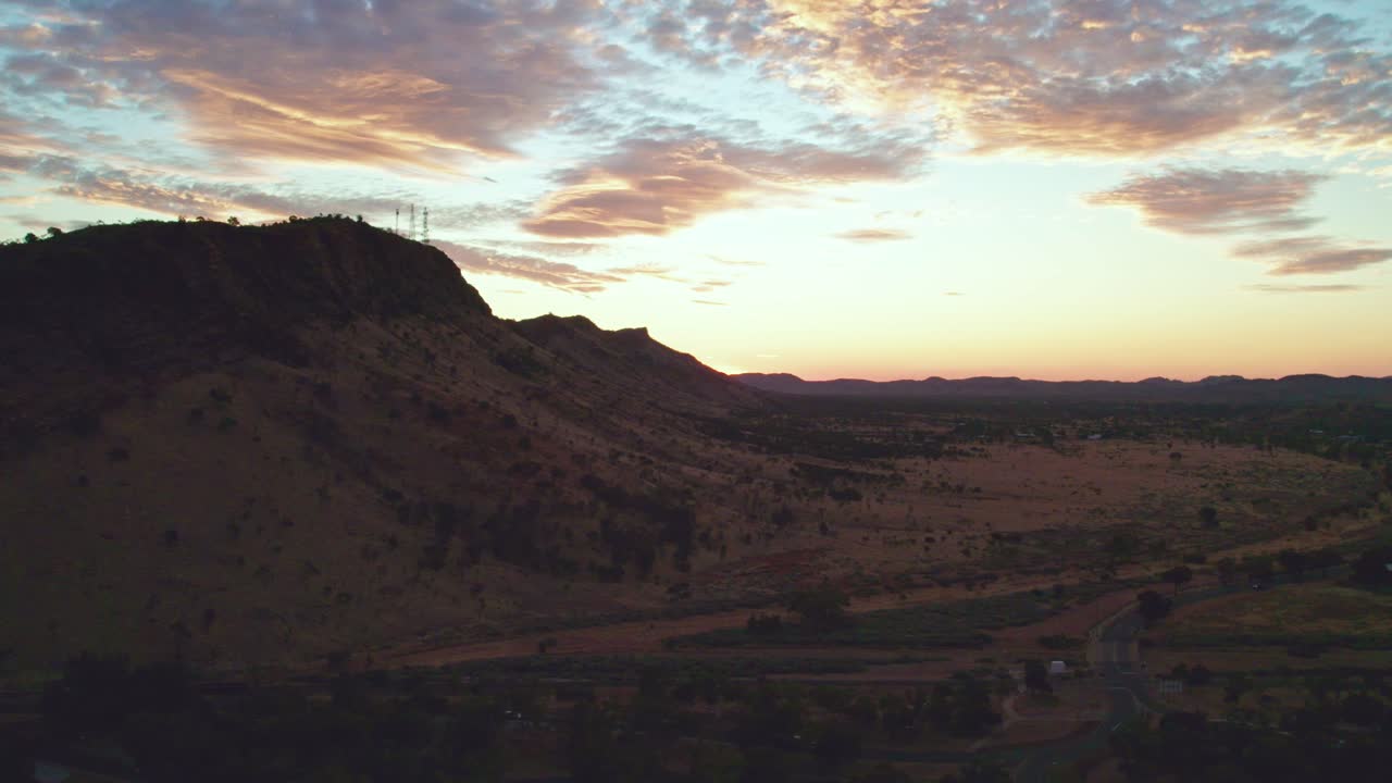 Rising drone footage of the MacDonnell Ranges near Heavitree Gap, Alice Springs, Mparntwe, with late afternoon behind the range. Northern Territory, Australia. August 2022.
