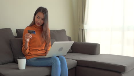 una mujer sentada en un sofá ingresa su número de tarjeta de crédito en su computadora portátil